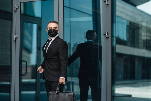再びcovid-19パンデミック後に動作するように。現代のオフィスビルに行く保護顔マスクの中年ビジネスマン - 写真・画像