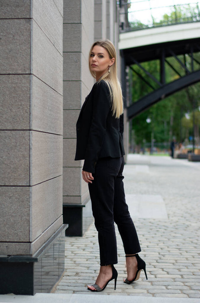 una mujer rubia en un traje de negocios negro en la ciudad.mujer de negocios en un paseo - Foto, Imagen