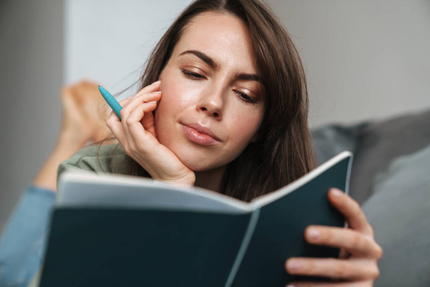 Young white woman reading her planner while lying on sofa at home - Φωτογραφία, εικόνα