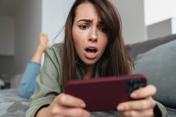 Unhappy caucasian woman playing online game on cellphone at home - Foto, imagen
