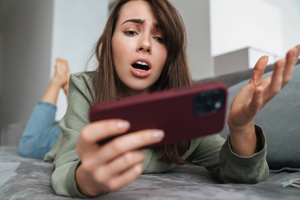 Unhappy caucasian woman playing online game on cellphone at home - Foto, imagen