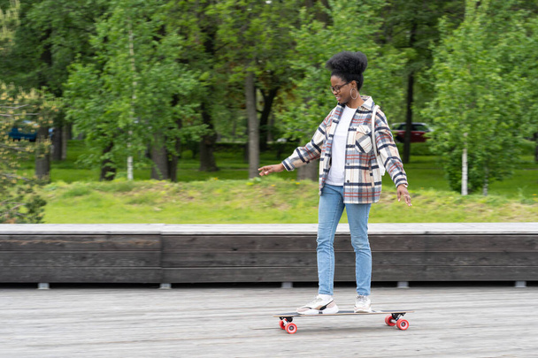 Катание на скейтборде и городской образ жизни: триумфальная африканская девочка на лонгборде в городском парке - Фото, изображение