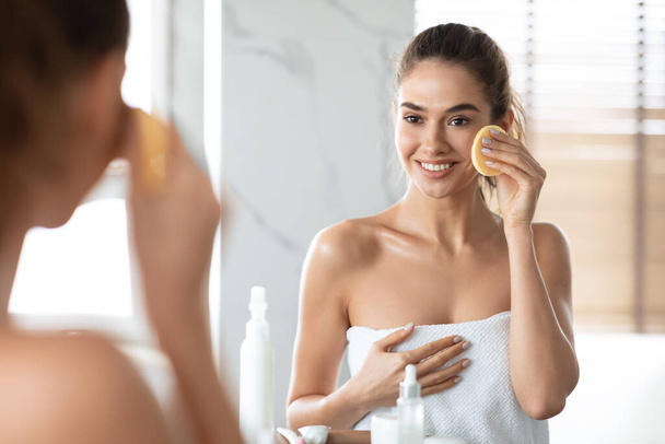 Kobieta za pomocą gąbki kosmetycznej Korzystanie pielęgnacji twarzy rutyny w łazience - Zdjęcie, obraz