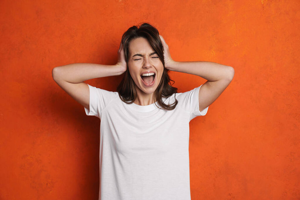 Irritated caucasian girl screaming while holding her head isolated over orange wall - Фото, зображення