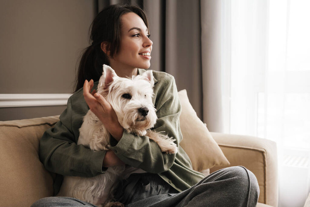 Happy white woman resting with her dog on sofa at home - Valokuva, kuva