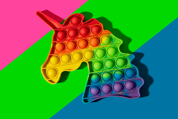 Novo brinquedo de silicone pop-lo em forma de unicórnio no neon fundo multicolorido. - Foto, Imagem
