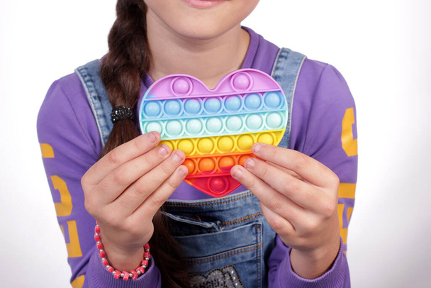 Νεαρό κορίτσι κρατώντας μια πολύχρωμη καρδιά σιλικόνης στα χέρια της. - Φωτογραφία, εικόνα