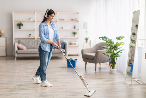 Mujer alegre escuchando música limpiar piso con fregona - Foto, imagen