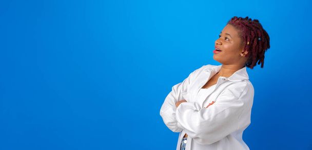 Young afro woman in white shirt looking up at copy space for advertising on blue background - Fotoğraf, Görsel