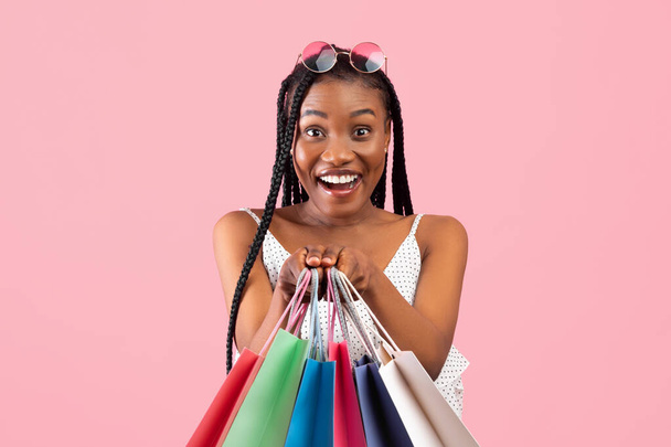 Encantadora jovem mulher negra com cachos afro segurando lotes de sacos de compras no fundo do estúdio rosa - Foto, Imagem