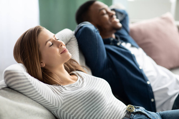リラックスコンセプト。若い異人種間のカップルが自宅で快適なソファで一緒に休憩 - 写真・画像