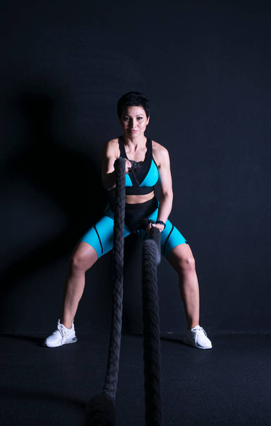 A brunette woman in a tracksuit performs physical exercises for the hands with ropes. Looks into the camera. - Foto, Imagem