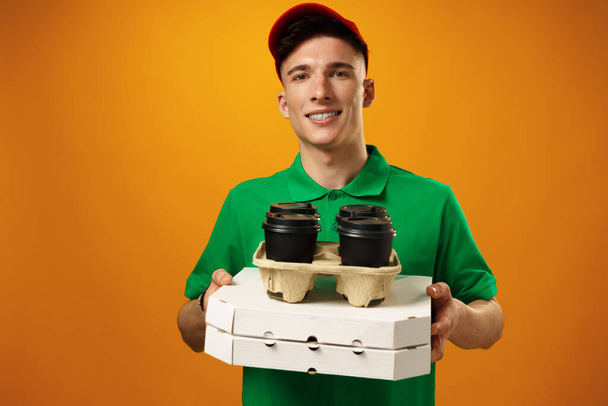 Happy young delivery man holding pizza box against yellow background - Foto, imagen