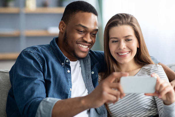 Happy Interracial Couple Watching Video Content On Smartphone While Relaxing At Home - Φωτογραφία, εικόνα