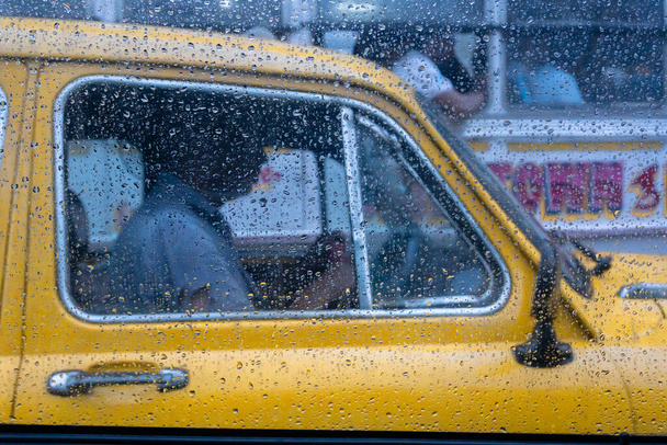 Raindrops falling on glass, abstract blurs - monsoon stock image of traditional yellow taxi of Kolkata (formerly Calcutta) city , West Bengal, India - Photo, Image