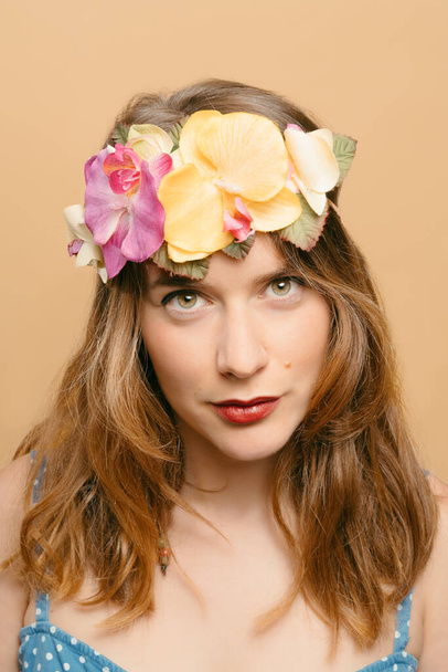 Retrato de una joven rubia con una tiara de flores y plantas en la cabeza mirando cámaras sobre un fondo amarillo. concepto de verano y naturaleza. imagen vertical con espacio de copia - Foto, Imagen