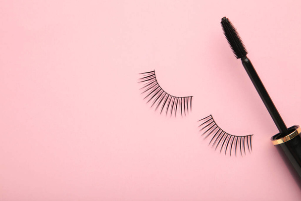 Black eyelashes and mascara on pink background with copy space. Beauty concept - 写真・画像