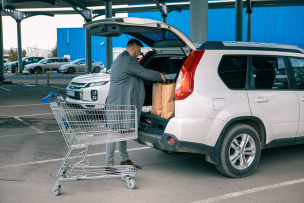 man putting bags with product in car trunk copy space - Foto, Imagen