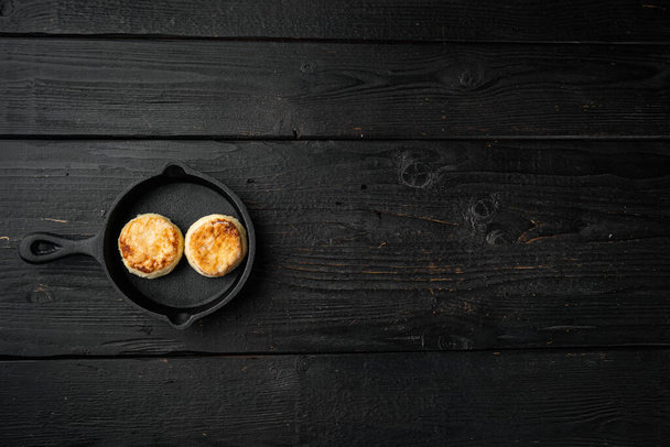 Panquecas de queijo cottage assadas definidas na frigideira de frigideira de ferro fundido, vista superior plana, no velho fundo de mesa de madeira escura, com espaço de cópia para texto - Foto, Imagem