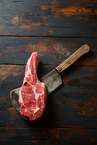 Raw Cowboy steak on meat cleaver. Organic farm marbled prime beef. Dark wooden background. Top view. Copy space. - Foto, Imagen