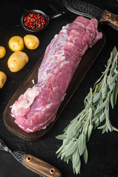Raw Pork fillet with sage set, on wooden cutting board, with barbeque knife and meat fork, on black stone background, top view flat lay - Foto, Imagen