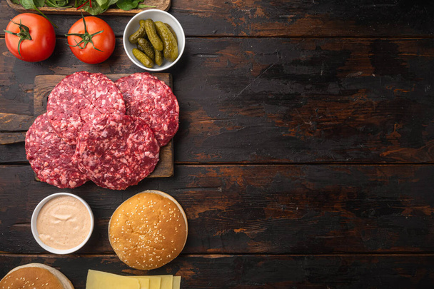 Ingredients for cooking burgers. Minced beef patties, buns, tomatoes, herbs and spices set, on old dark  wooden table background, top view flat lay, with copy space for text - Foto, imagen