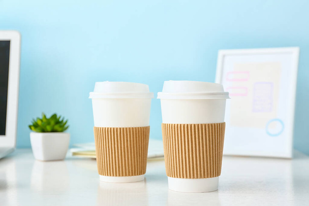 Tazas para llevar para café en la mesa cerca de la pared de color - Foto, Imagen