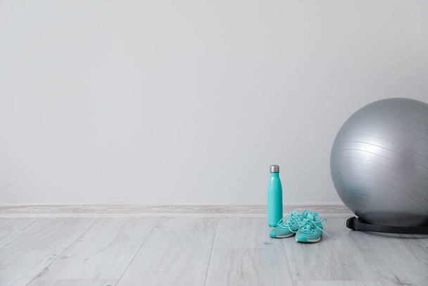 Fitness ball, bottle and shoes near light wall - 写真・画像