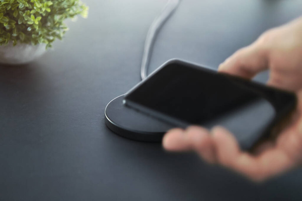 Need to recharge smartphone battery. Male hand laying down electronic device on wireless charger. Modern technology, wireless device and transfer of energy concept. - Photo, Image