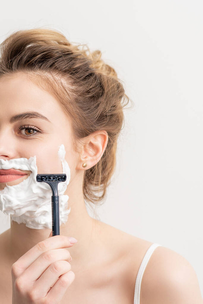 Beautiful young caucasian smiling woman shaving her face with razor on white background - Photo, Image