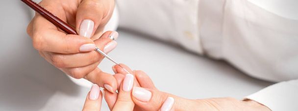 Franse manicure. Manicure master tekening witte vernis op de nagel tip met een dunne borstel, close-up - Foto, afbeelding