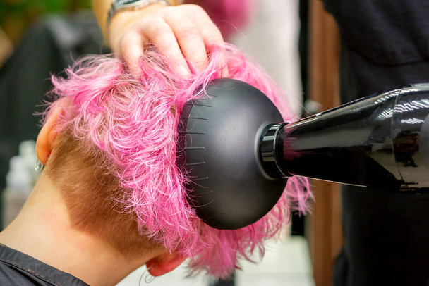 Un profesional de peluquería masculina secado elegante pelo rosa de la cliente femenina con un secador de pelo en un salón de belleza - Foto, Imagen
