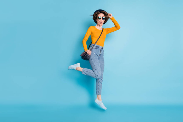 Full size profile photo of optimistic brunette short hairdo lady jump with bag wear shirt jeans sneakers isolated on blue color background - Fotografie, Obrázek