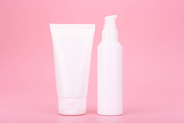 Two white cosmetic bottles with cream, lotion or scrub for face or hands on pink background - Фото, изображение