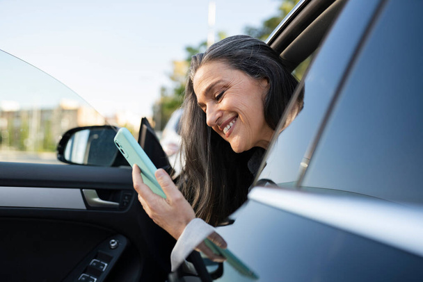 mature woman, businesswoman getting out of car using smartphone - Foto, imagen
