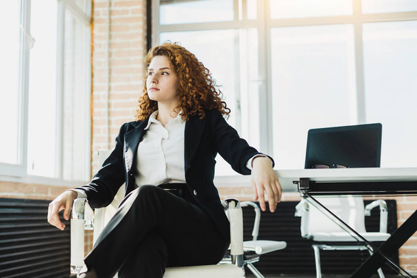 Portrait of a beautiful young business woman with red curly hair working productively in the office. Successful career and staff of a large company - Fotó, kép