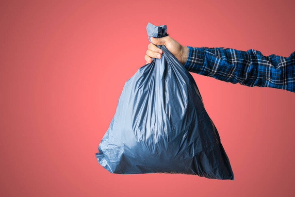 a hand holding the dark blue trash bag, concept of cleaning earth planet,isolated against the colored wall, simple concept - Foto, imagen