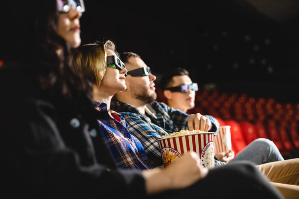 Friends are watching a movie in the cinema. People sit in the armchairs of the cinema and look at the screen with special glasses for 3D - Foto, imagen