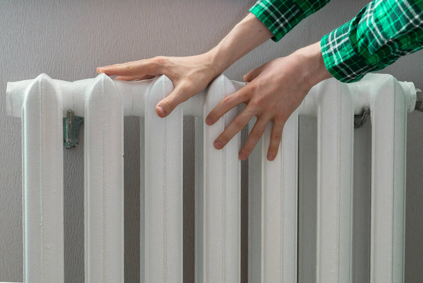 the frozen hands touch a heating battery at home during winter season - Photo, Image
