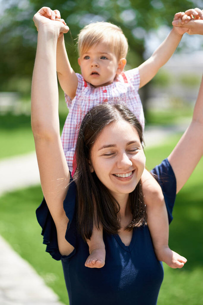 Mãe feliz carrega uma menina em seus ombros segurando suas mãos - Foto, Imagem