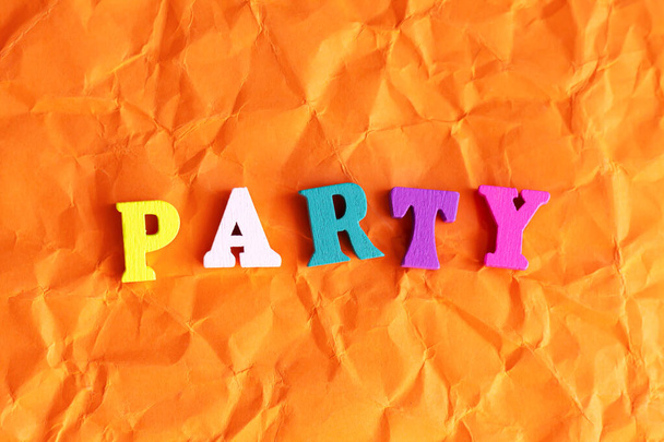 Text "Party" mit bunten Holzbuchstaben auf zerknittertem orangefarbenem Hintergrund. Festkonzept - Foto, Bild
