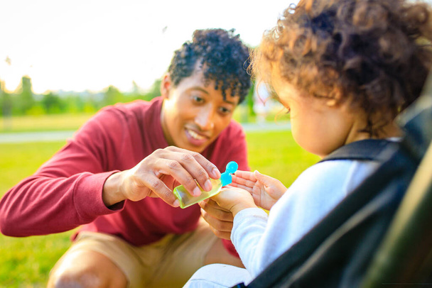 african american father and lirrle girl are useing an ntibacterial gel in summer park outdoors - Фото, зображення