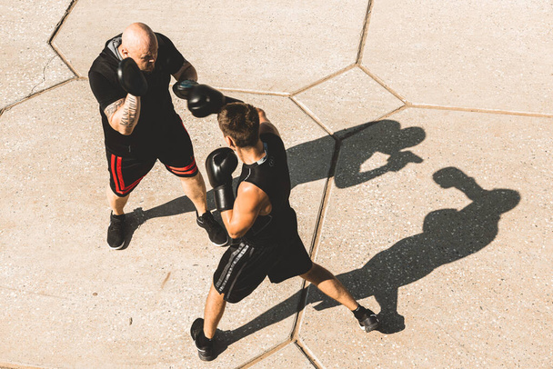 Two men exercising and fighting in outside. Boxer in gloves is training with a coach - Photo, Image