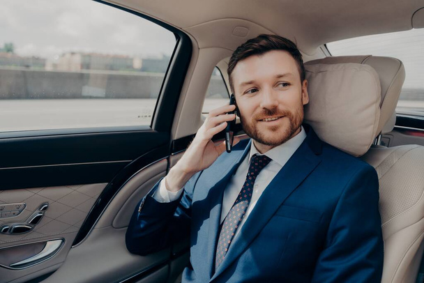Young good looking businessman taking ride to conference while talking on phone - Photo, Image