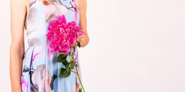 a young woman in a colorful dress with a peony flower in her hand on a light pink background with a copy space - Photo, image