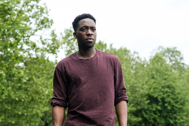 Портрет молодого черного мужчины в парке. На нем красный свитер.. - Фото, изображение
