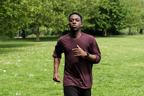 Młody czarny mężczyzna biegający w parku. Ma na sobie czerwony sweter.. - Zdjęcie, obraz