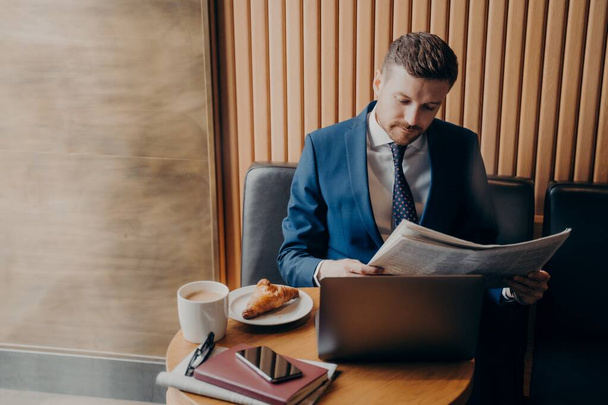 Fiatal férfi vállalkozó hivatalos szmokingban újságot olvas a kávézóban - Fotó, kép