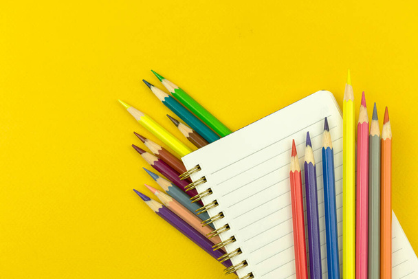 メモ帳とカラー図面鉛筆、教育の概念、黄色のデスクトップの背景、トップビューを持つ学校の組成に戻る  - 写真・画像