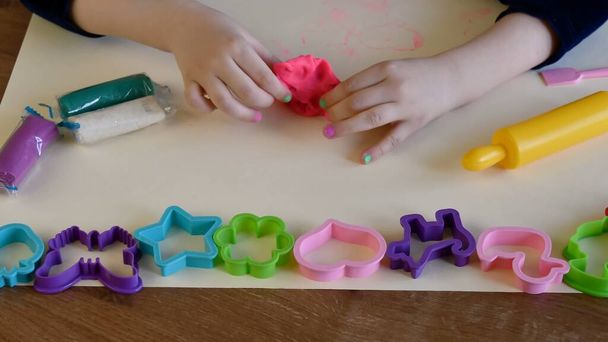 Παιδικά χέρια παίζουν πολύχρωμο παιχνίδι ζύμης με πλαστικά καλούπια και πλάστη τροχαίο - Φωτογραφία, εικόνα